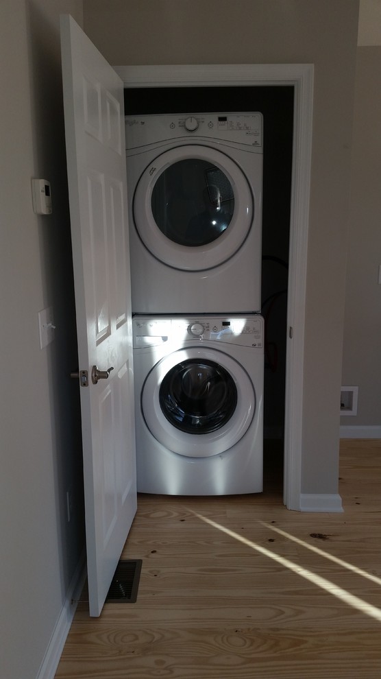 Imagen de armario lavadero clásico pequeño con lavadora y secadora apiladas, paredes blancas y suelo de madera clara