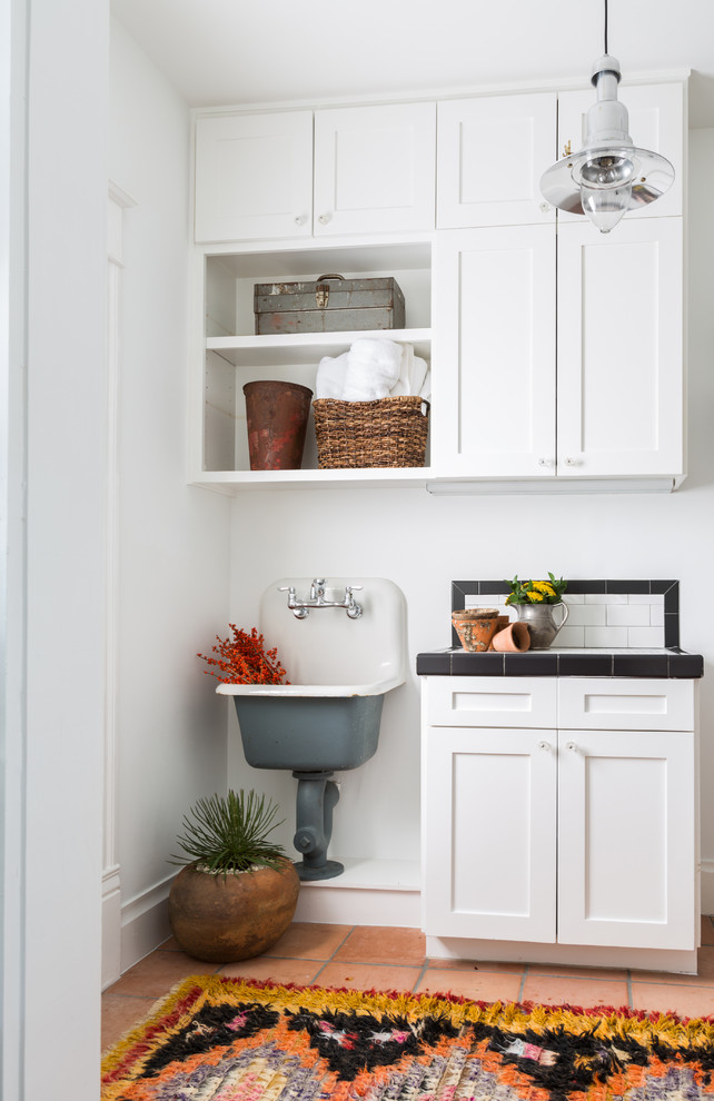 Inspiration for an utility room in Houston with a single-bowl sink, shaker cabinets, white cabinets, tile countertops, white walls and terracotta flooring.