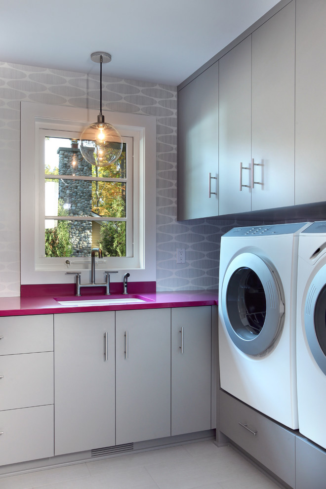 Exempel på ett stort modernt rosa l-format rosa grovkök, med en tvättmaskin och torktumlare bredvid varandra, en undermonterad diskho, släta luckor, grå skåp, laminatbänkskiva, grå väggar, klinkergolv i keramik och grått golv