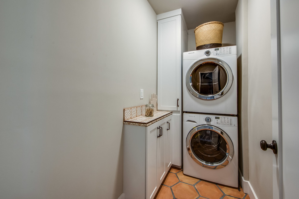 Ejemplo de armario lavadero mediterráneo con armarios estilo shaker, puertas de armario blancas, encimera de azulejos, paredes verdes, suelo de baldosas de terracota, lavadora y secadora apiladas y suelo naranja