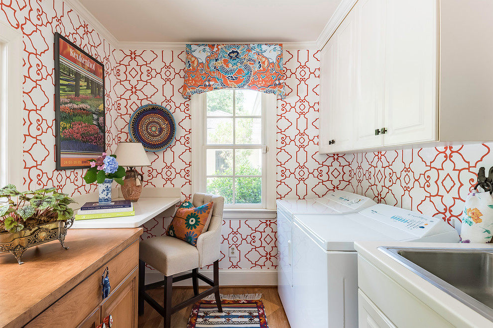 Inredning av en klassisk liten parallell tvättstuga, med bänkskiva i koppar, en tvättmaskin och torktumlare bredvid varandra, luckor med upphöjd panel, en nedsänkt diskho, vita skåp, röda väggar, mellanmörkt trägolv och brunt golv