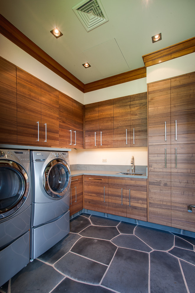Modelo de lavadero tropical con armarios con paneles lisos, puertas de armario de madera oscura, lavadora y secadora juntas y suelo gris