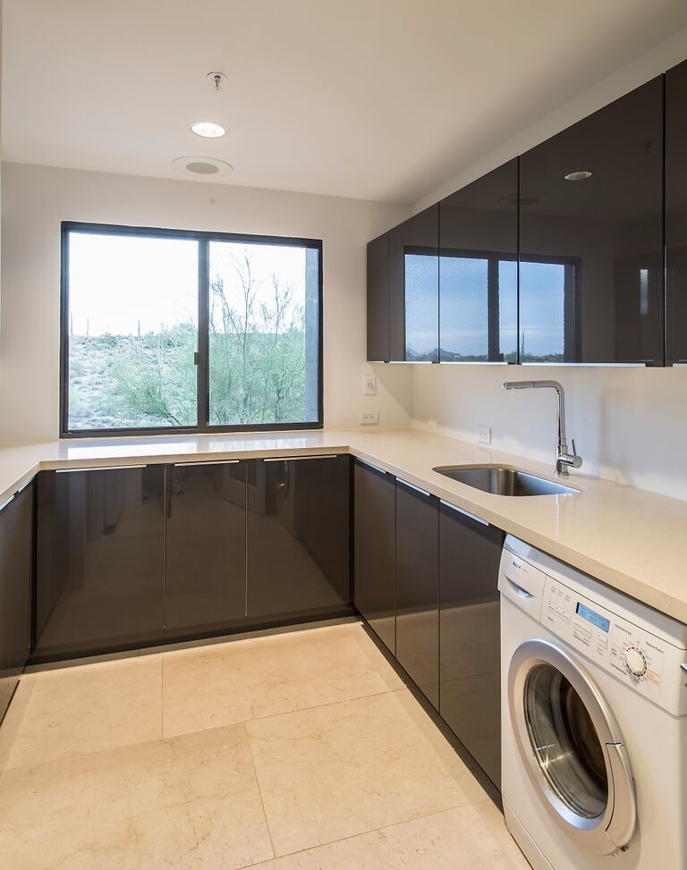 Photo of a medium sized modern u-shaped utility room in Phoenix with a submerged sink, flat-panel cabinets, brown cabinets, composite countertops, white walls, ceramic flooring, a side by side washer and dryer and beige floors.