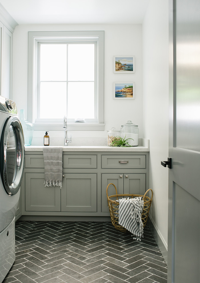 Ejemplo de cuarto de lavado en L costero con puertas de armario grises, paredes blancas, suelo gris, encimeras blancas y armarios con rebordes decorativos