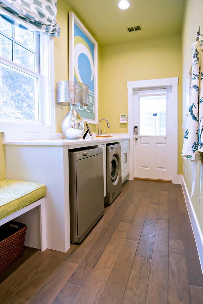 ジャクソンビルにある高級な広いトロピカルスタイルのおしゃれな洗濯室 (ll型、落し込みパネル扉のキャビネット、白いキャビネット、黄色い壁、濃色無垢フローリング、左右配置の洗濯機・乾燥機) の写真