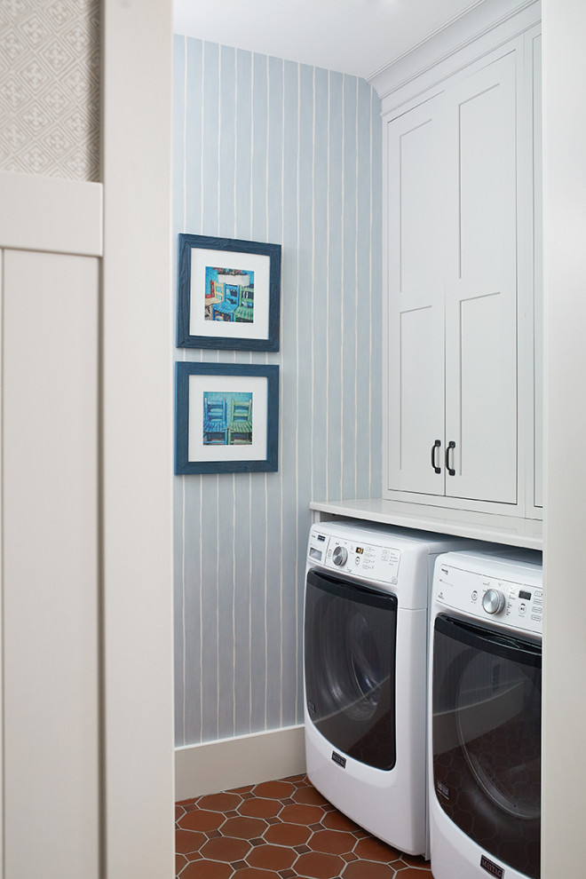 Maritim inredning av en liten parallell tvättstuga enbart för tvätt, med vita skåp, flerfärgade väggar, klinkergolv i keramik, en tvättmaskin och torktumlare bredvid varandra, brunt golv och skåp i shakerstil