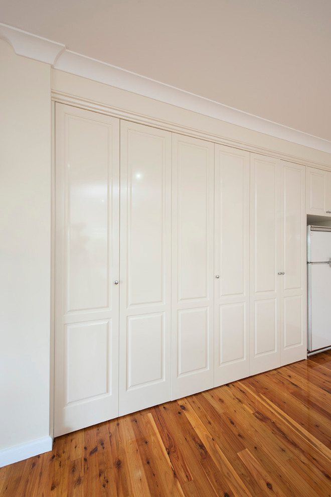 Large elegant single-wall medium tone wood floor laundry closet photo in Melbourne with a drop-in sink, white cabinets, laminate countertops, white walls and a concealed washer/dryer
