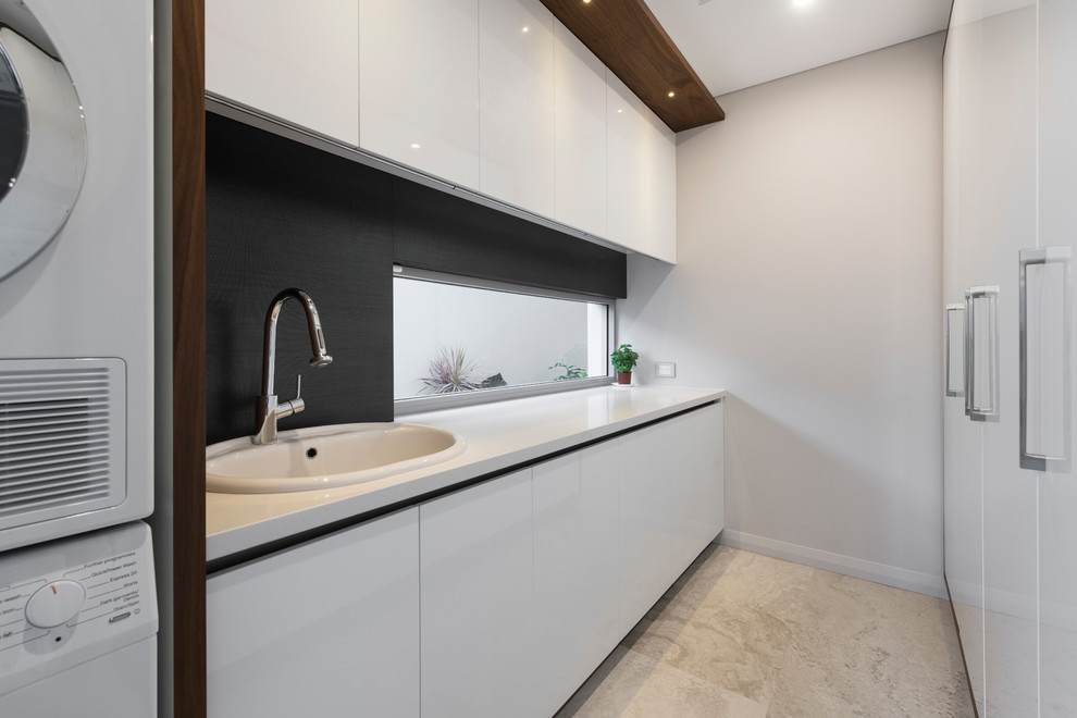 Modern inredning av en stor vita parallell vitt tvättstuga enbart för tvätt, med en nedsänkt diskho, luckor med infälld panel, vita skåp, bänkskiva i kvarts, grå väggar, en tvättpelare, grått golv och kalkstensgolv