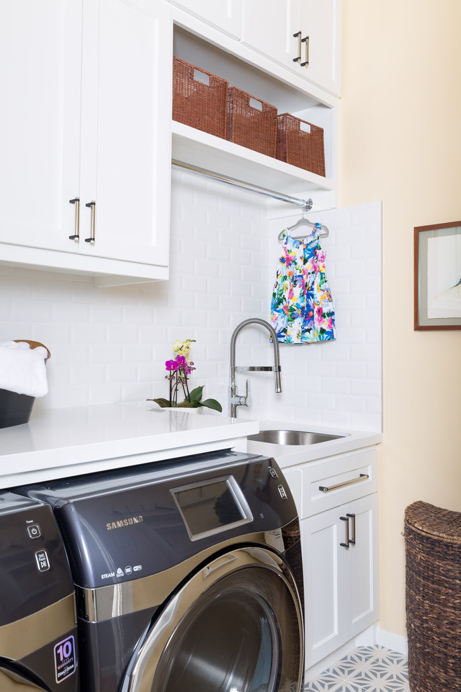 ヒューストンにある高級な中くらいなコンテンポラリースタイルのおしゃれな洗濯室 (I型、アンダーカウンターシンク、シェーカースタイル扉のキャビネット、白いキャビネット、クオーツストーンカウンター、オレンジの壁、左右配置の洗濯機・乾燥機、白いキッチンカウンター) の写真