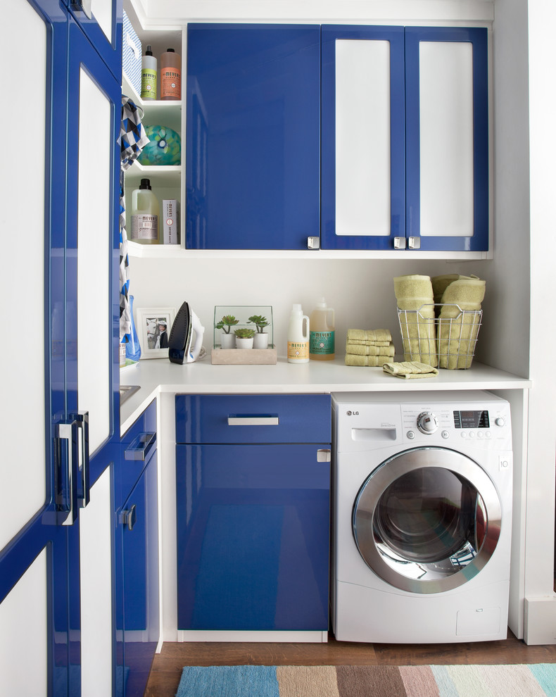 Ejemplo de lavadero multiusos y en L minimalista pequeño con fregadero encastrado, armarios con paneles lisos, puertas de armario azules, encimera de laminado, paredes blancas, suelo de madera en tonos medios y lavadora y secadora integrada