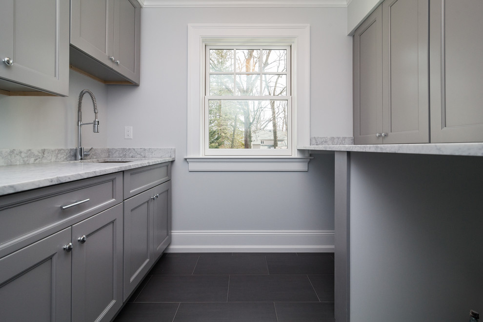 Inspiration for a mid-sized transitional single-wall porcelain tile dedicated laundry room remodel in New York with an undermount sink, shaker cabinets, gray cabinets, marble countertops and gray walls