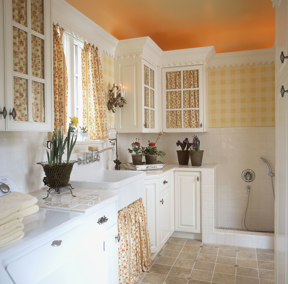 Exempel på ett klassiskt grovkök, med en rustik diskho, luckor med glaspanel, vita skåp, kaklad bänkskiva, gula väggar och en tvättmaskin och torktumlare bredvid varandra
