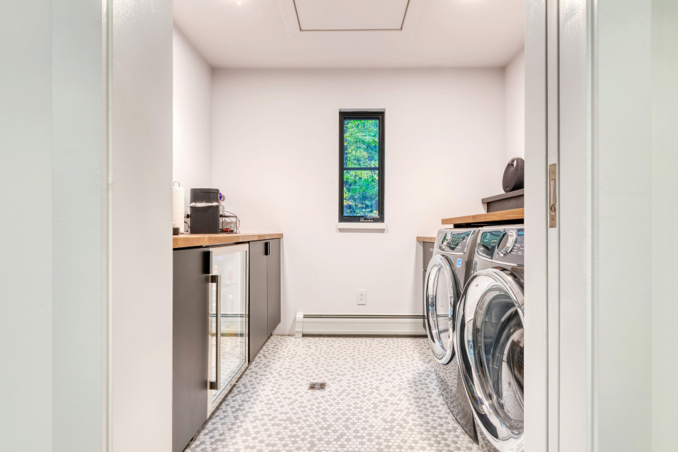 Exempel på en liten modern parallell tvättstuga enbart för tvätt, med en nedsänkt diskho, släta luckor, svarta skåp, träbänkskiva, vita väggar, klinkergolv i keramik, en tvättmaskin och torktumlare bredvid varandra och flerfärgat golv