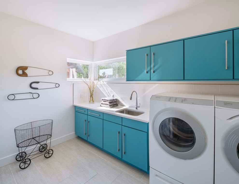 Einzeilige Moderne Waschküche mit Unterbauwaschbecken, flächenbündigen Schrankfronten, blauen Schränken, weißer Wandfarbe, hellem Holzboden, Waschmaschine und Trockner nebeneinander und weißer Arbeitsplatte in Austin