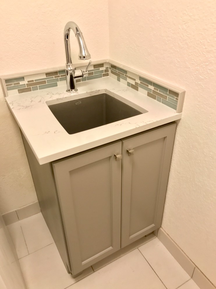 Inspiration for a mid-sized timeless u-shaped porcelain tile and white floor dedicated laundry room remodel in Portland with an undermount sink, recessed-panel cabinets, gray cabinets, quartz countertops, white walls and a stacked washer/dryer