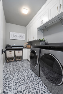 Classic cottage laundry room features a white and gray granite countertop  positioned over a sil…