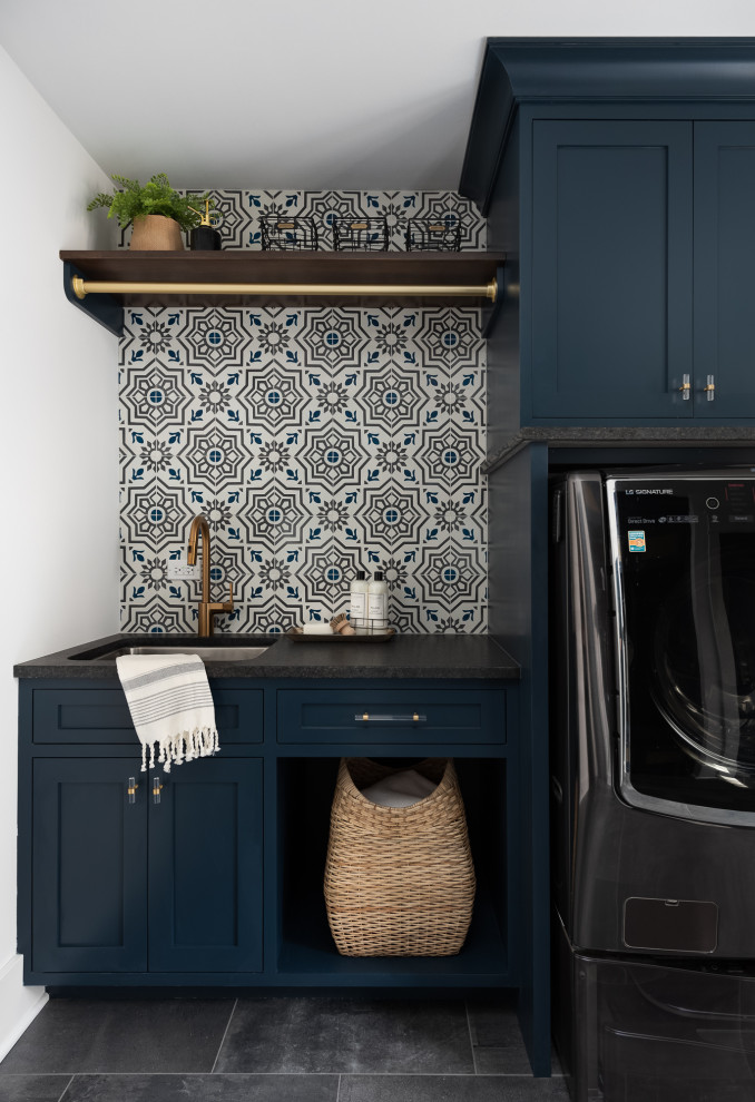 Idee per una lavanderia country con lavello sottopiano, ante in stile shaker, ante blu, paraspruzzi multicolore, pareti bianche, pavimento grigio e top nero