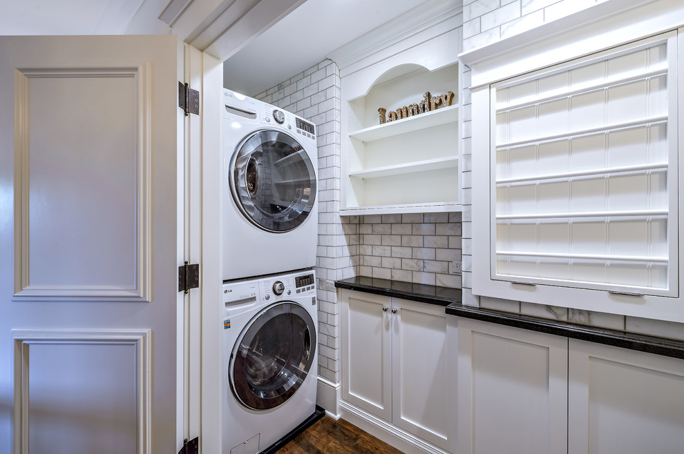This is an example of a medium sized traditional l-shaped utility room in San Diego with a belfast sink, shaker cabinets, white cabinets, beige walls, medium hardwood flooring, a stacked washer and dryer, brown floors and black worktops.