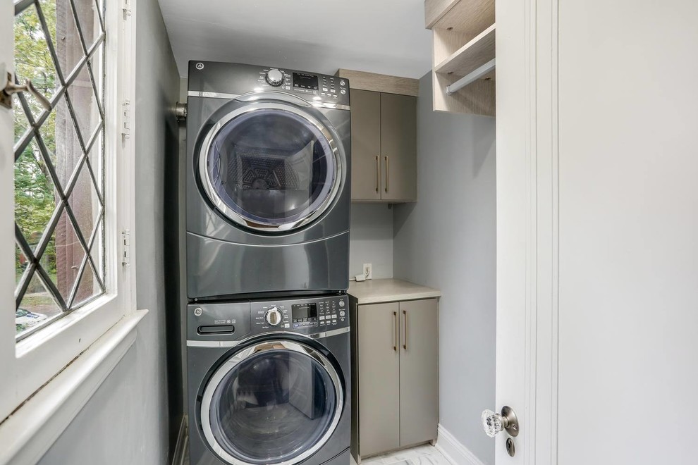 Klassisk inredning av en liten grå linjär grått tvättstuga enbart för tvätt, med släta luckor, grå skåp, träbänkskiva, grå väggar, marmorgolv, en tvättpelare och vitt golv