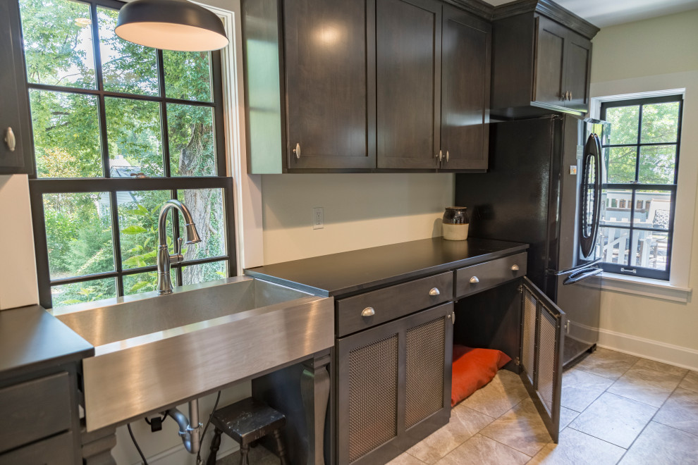 This is an example of a medium sized traditional single-wall utility room in St Louis with an utility sink, shaker cabinets, dark wood cabinets, beige walls, a stacked washer and dryer, grey floors and black worktops.