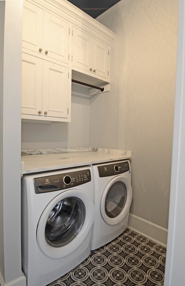 Bild på en stor vintage vita vitt tvättstuga, med luckor med profilerade fronter, grå skåp, granitbänkskiva, klinkergolv i porslin, en tvättmaskin och torktumlare bredvid varandra och grått golv