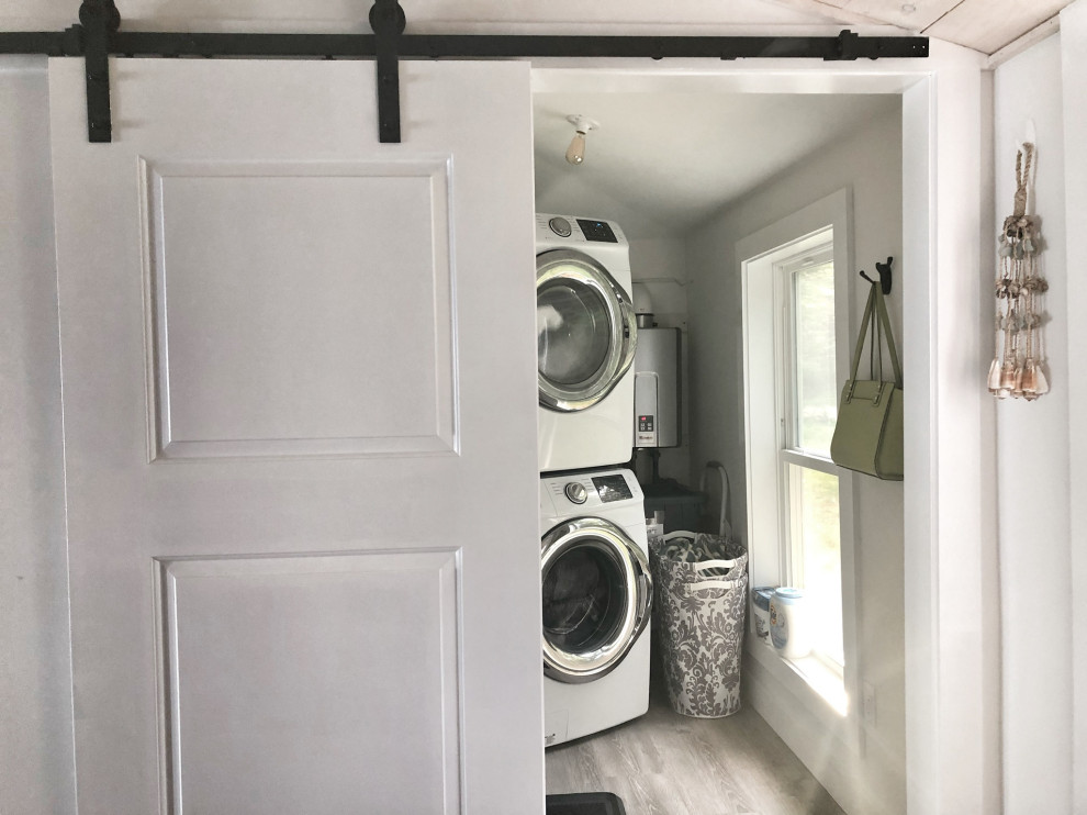 Design ideas for a small coastal single-wall laundry cupboard in Portland Maine with white walls, laminate floors, a stacked washer and dryer and grey floors.