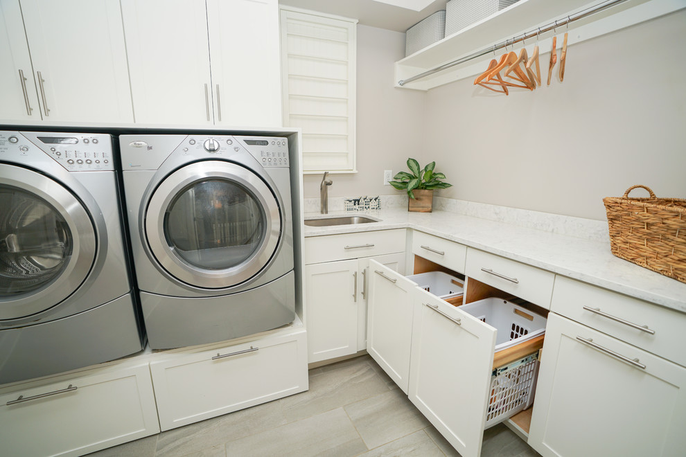 Idéer för en mellanstor klassisk l-formad tvättstuga enbart för tvätt, med en undermonterad diskho, luckor med infälld panel, vita skåp, marmorbänkskiva, grå väggar, klinkergolv i keramik, en tvättmaskin och torktumlare bredvid varandra och grått golv