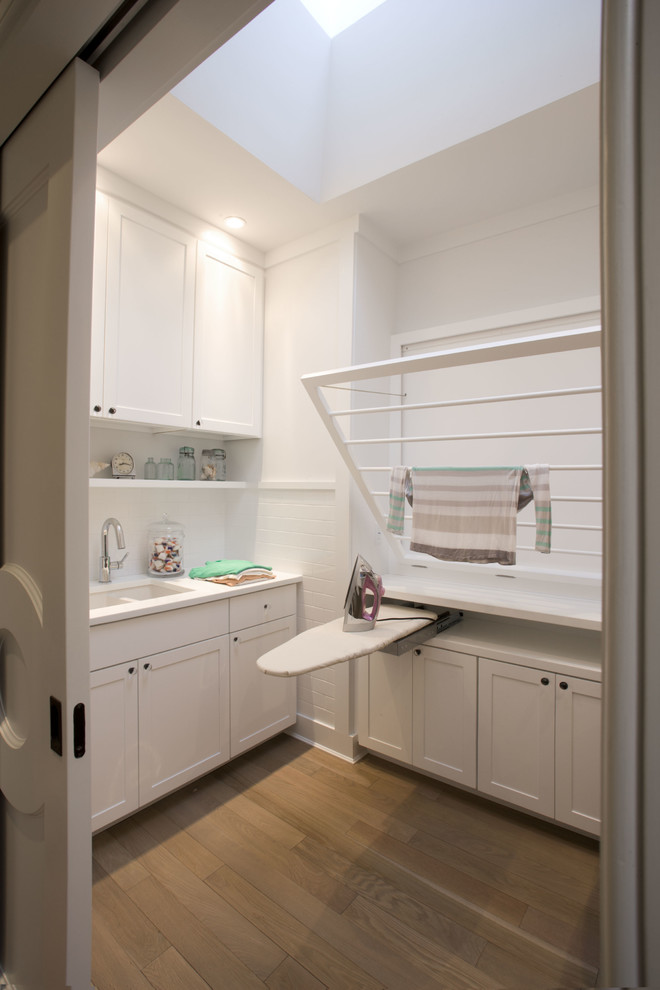 Diseño de cuarto de lavado tradicional renovado con fregadero bajoencimera, armarios con paneles empotrados, puertas de armario blancas, paredes blancas y suelo de madera clara
