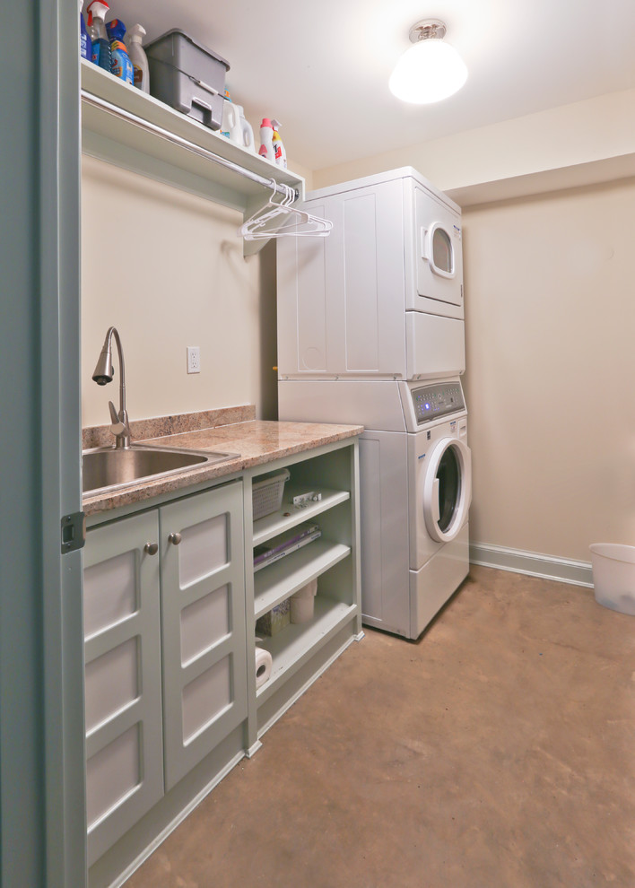 Modelo de cuarto de lavado lineal vintage grande con fregadero encastrado, armarios con rebordes decorativos, suelo de cemento y lavadora y secadora apiladas