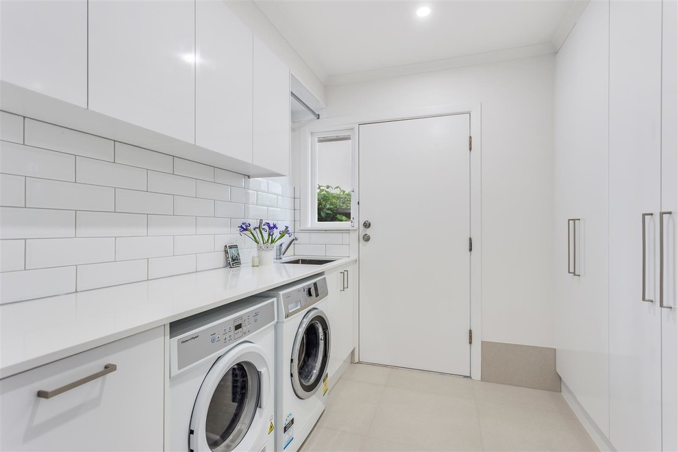 Design ideas for a medium sized contemporary galley separated utility room in Gold Coast - Tweed with a submerged sink, flat-panel cabinets, white cabinets, quartz worktops, white walls, a side by side washer and dryer, grey floors and white worktops.