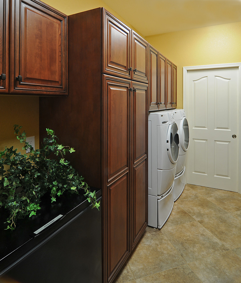 Esempio di una lavanderia multiuso tradizionale di medie dimensioni con ante con bugna sagomata, pareti gialle, pavimento con piastrelle in ceramica, lavatrice e asciugatrice affiancate e ante in legno bruno
