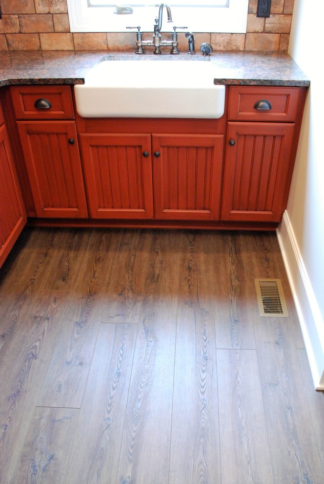 Trendy vinyl floor and brown floor laundry room photo in Cleveland with a farmhouse sink, shaker cabinets, medium tone wood cabinets and granite countertops