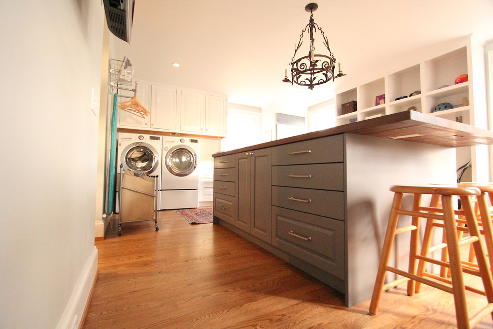 This is an example of a large classic l-shaped utility room in Other with a built-in sink, raised-panel cabinets, white cabinets, wood worktops, grey walls, medium hardwood flooring, a side by side washer and dryer and brown floors.