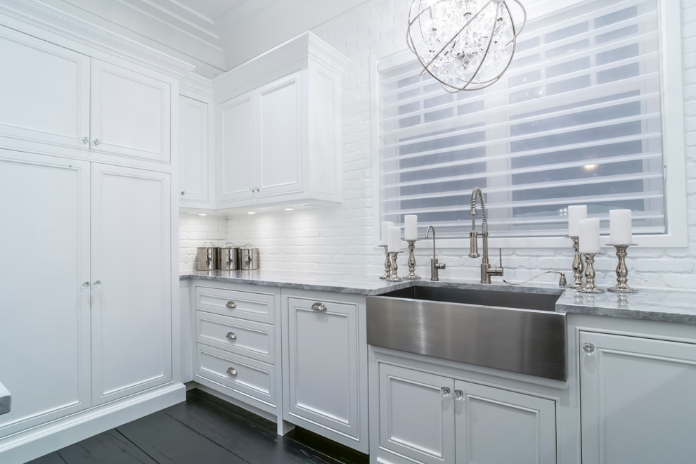 This is an example of a classic single-wall separated utility room in Edmonton with beaded cabinets, white cabinets, white walls, dark hardwood flooring, a stacked washer and dryer and a belfast sink.