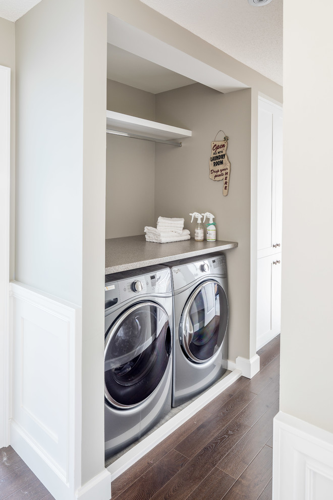 Design ideas for an expansive classic single-wall laundry cupboard in Toronto with a belfast sink, shaker cabinets, white cabinets, laminate countertops, beige walls, laminate floors, a side by side washer and dryer, brown floors and grey worktops.