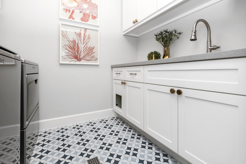 Foto på en mellanstor vintage grå tvättstuga enbart för tvätt, med en undermonterad diskho, vita skåp, granitbänkskiva, vitt stänkskydd, stänkskydd i keramik, grå väggar, klinkergolv i keramik, en tvättmaskin och torktumlare bredvid varandra och flerfärgat golv
