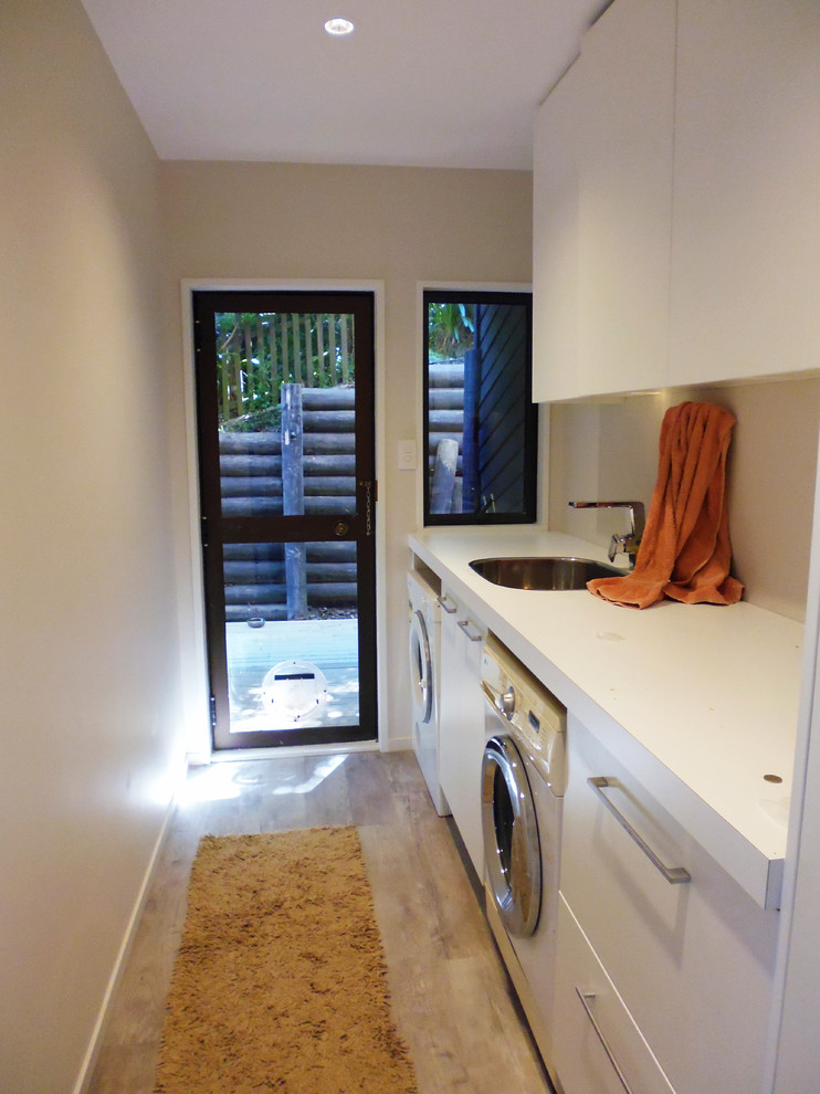 Example of a small classic galley linoleum floor dedicated laundry room design in Christchurch with a single-bowl sink and beige walls