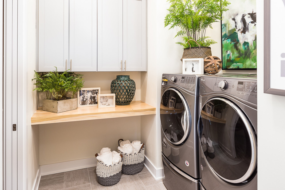Bild på en mellanstor vintage l-formad tvättstuga enbart för tvätt, med skåp i shakerstil, grå skåp, träbänkskiva, en tvättmaskin och torktumlare bredvid varandra, vita väggar, klinkergolv i keramik och grått golv