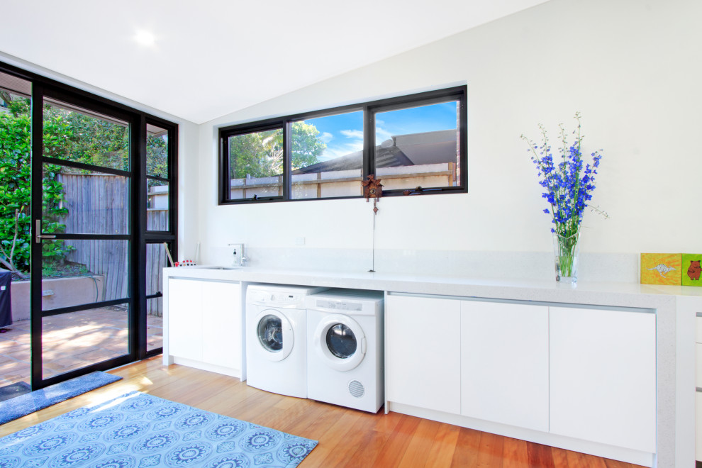 Large contemporary single-wall utility room in Sydney with an integrated sink, flat-panel cabinets, white cabinets, engineered stone countertops, grey splashback, beige walls, medium hardwood flooring, brown floors and grey worktops.