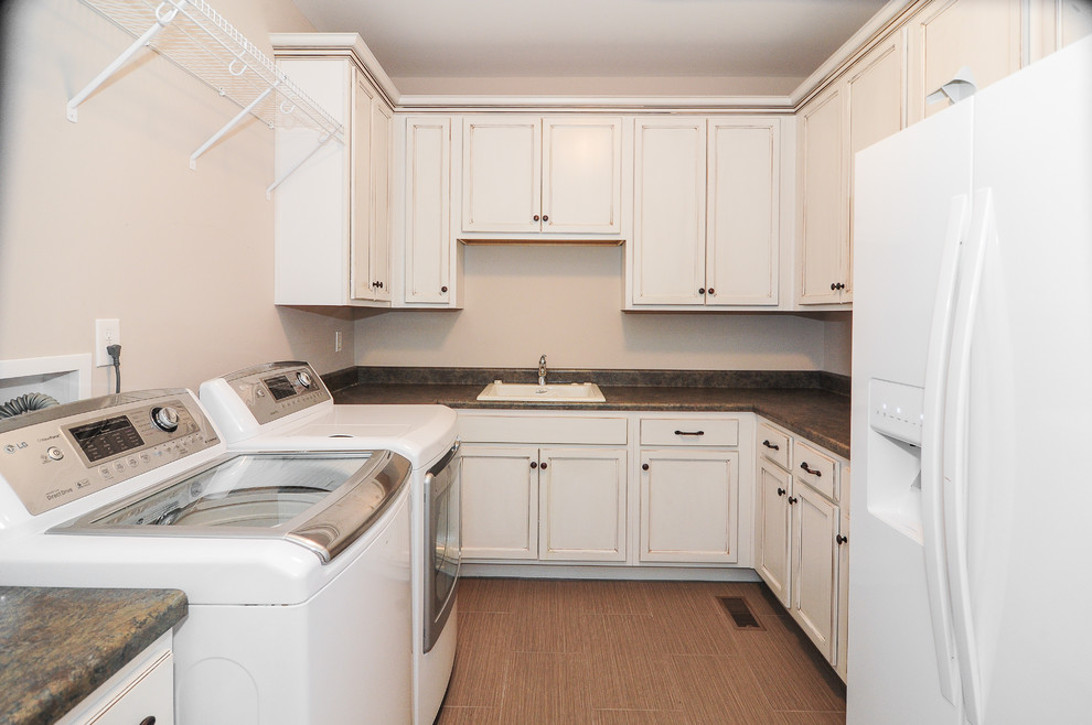 Example of a large classic u-shaped porcelain tile dedicated laundry room design in Birmingham with a drop-in sink, recessed-panel cabinets, distressed cabinets, granite countertops, white walls and a side-by-side washer/dryer