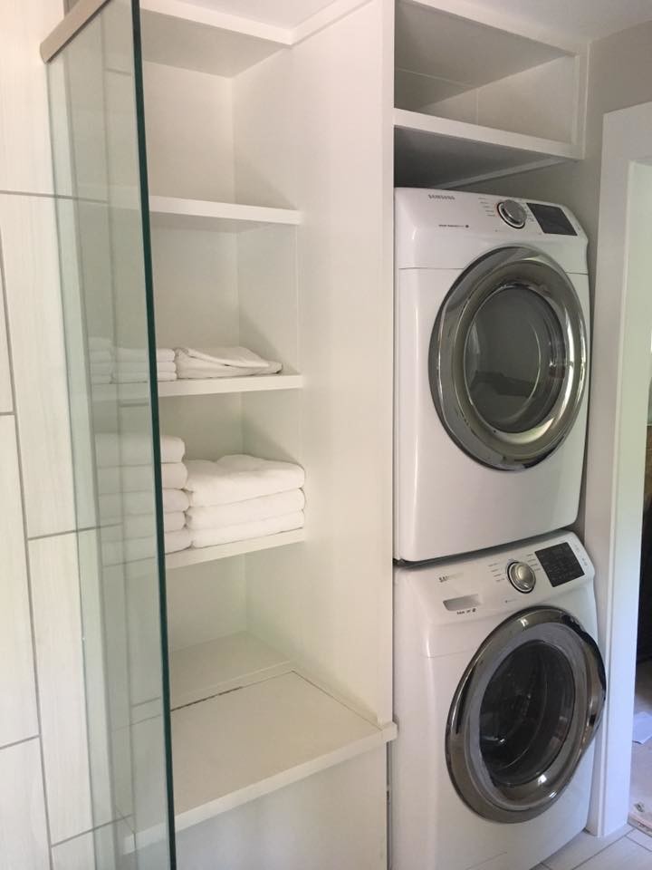 Small contemporary laundry cupboard in Birmingham with white cabinets, white walls, ceramic flooring, a stacked washer and dryer and white floors.