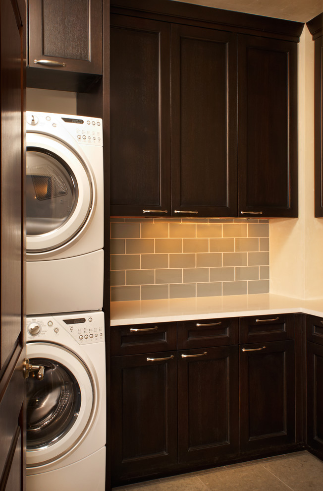 Example of a mid-sized trendy l-shaped limestone floor dedicated laundry room design in Denver with recessed-panel cabinets, quartz countertops, white walls and a stacked washer/dryer