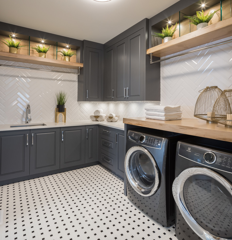 Example of a large trendy l-shaped porcelain tile and multicolored floor dedicated laundry room design in Calgary with an undermount sink, shaker cabinets, gray cabinets, wood countertops, white walls, a side-by-side washer/dryer and brown countertops