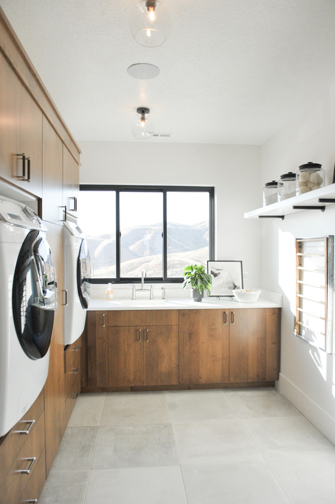 Inspiration for a contemporary l-shaped utility room in Salt Lake City with an integrated sink, flat-panel cabinets, white walls, a side by side washer and dryer, grey floors, white worktops and medium wood cabinets.