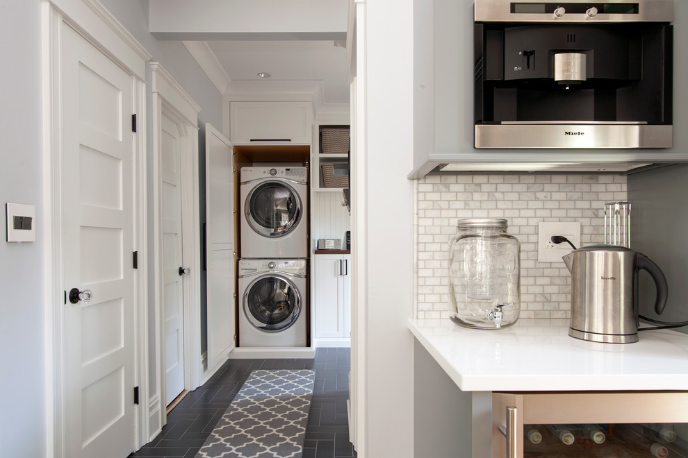 Photo of a classic utility room in New York with shaker cabinets, white cabinets, grey walls and a stacked washer and dryer.
