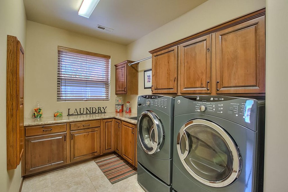 Dedicated laundry room - southwestern l-shaped limestone floor dedicated laundry room idea in Albuquerque with an undermount sink, raised-panel cabinets, medium tone wood cabinets, granite countertops, beige walls and a side-by-side washer/dryer