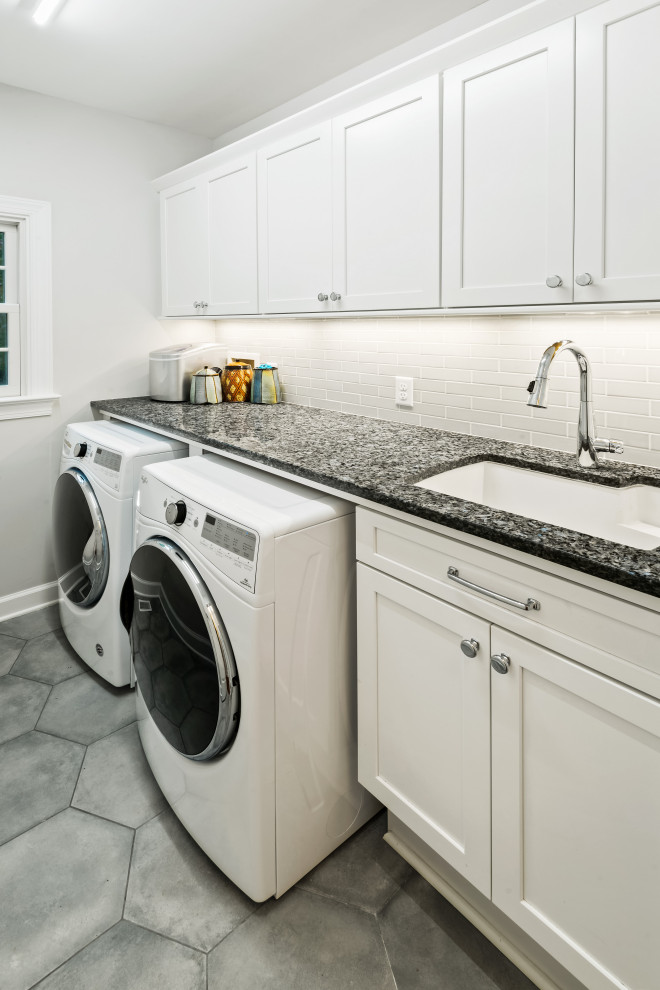 Exempel på en mellanstor klassisk grå linjär grått tvättstuga enbart för tvätt, med en undermonterad diskho, skåp i shakerstil, vita skåp, granitbänkskiva, grå väggar, klinkergolv i porslin, en tvättmaskin och torktumlare bredvid varandra och grått golv