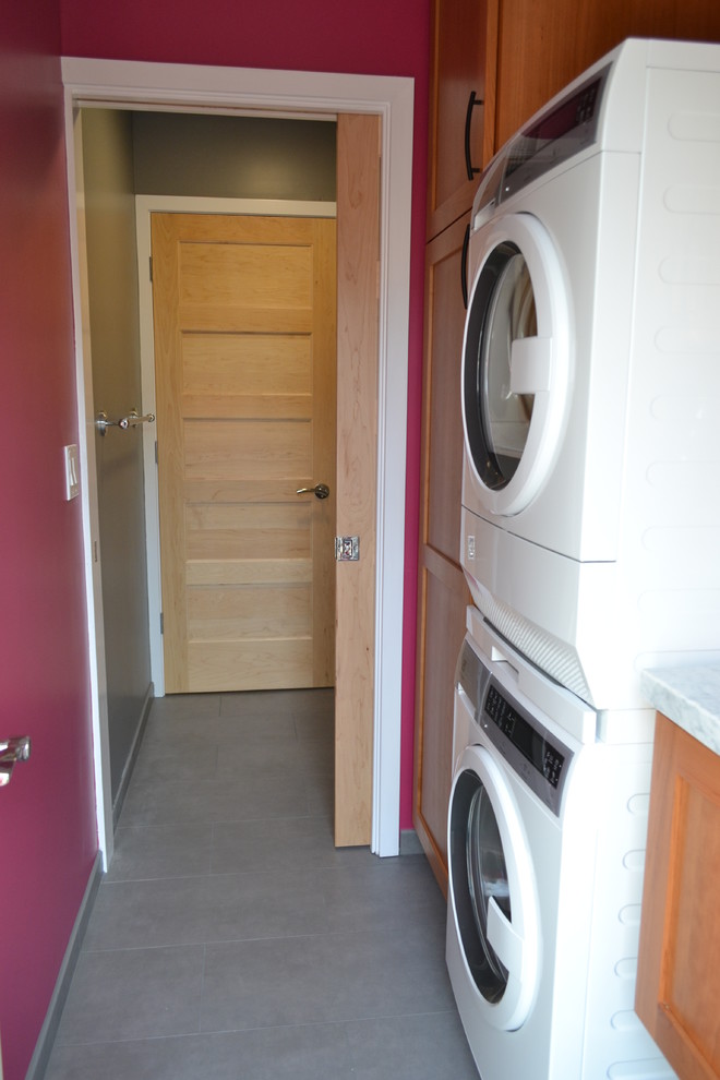 Example of a small trendy single-wall porcelain tile utility room design in San Francisco with an undermount sink, shaker cabinets, dark wood cabinets, granite countertops, pink walls and a stacked washer/dryer