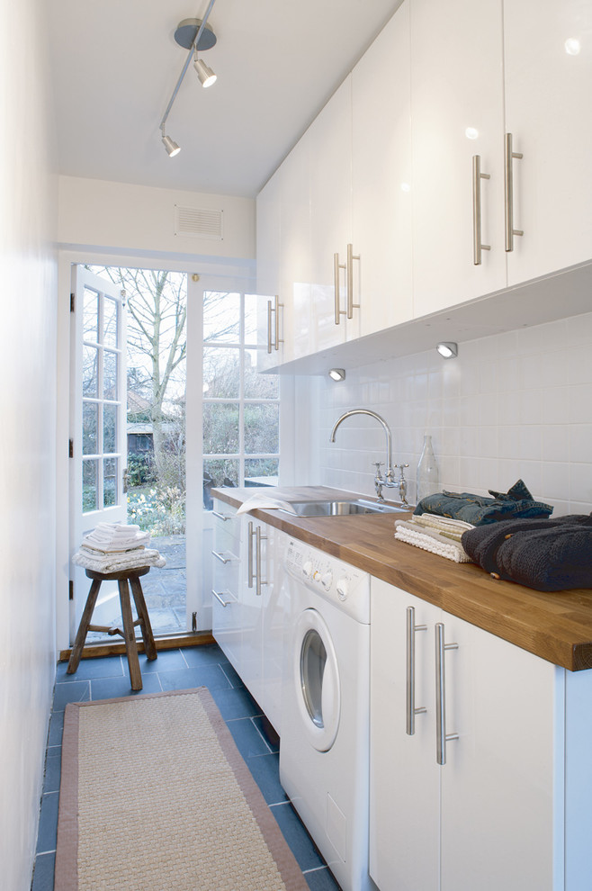 Example of a trendy single-wall dedicated laundry room design in Venice with a drop-in sink, flat-panel cabinets, white cabinets, wood countertops, white walls and brown countertops