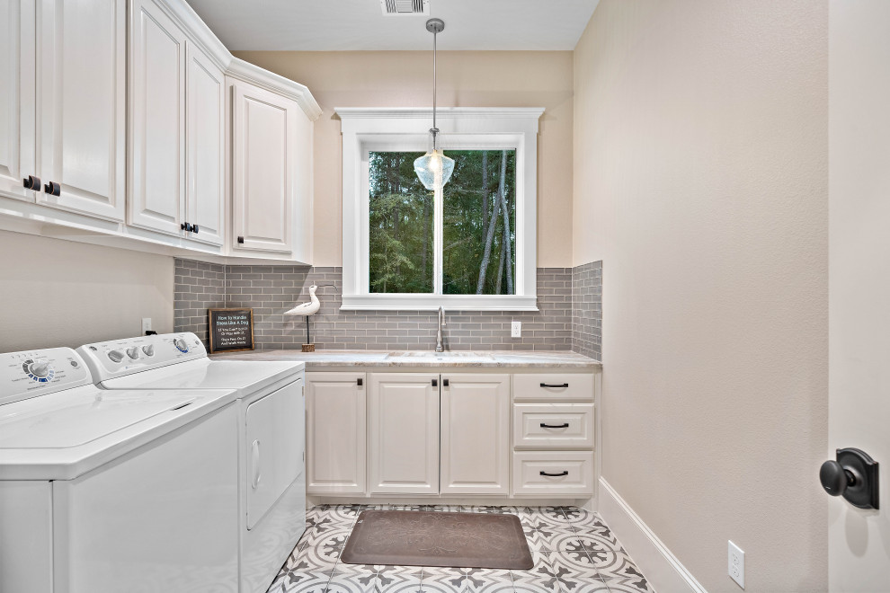 Immagine di una sala lavanderia con lavello sottopiano, ante con bugna sagomata, ante beige, pareti beige, lavatrice e asciugatrice affiancate, pavimento grigio e top beige